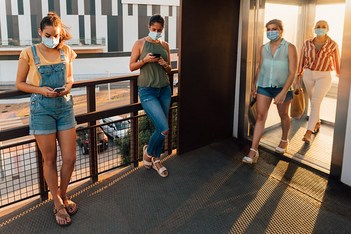 Young women with face mask waiting and exiting an outdoor elevator near a shopping mall