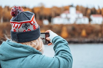 Woman photographer on a boat takes photos with her smart phone of a lighthouse, intentionally blurred in background.