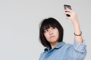 Cute Asian teenager using cellphone for selfie.